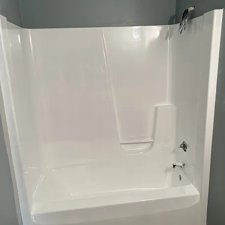 Refinished white bathtub and shower surround with glossy wall panels and built-in shelf
