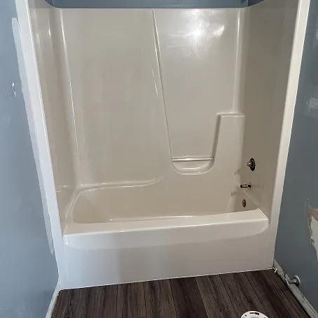 Refinished white bathtub and shower surround with glossy wall panels and built-in shelf