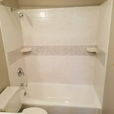 White bathtub and shower with textured wall surround and built-in corner shelves.